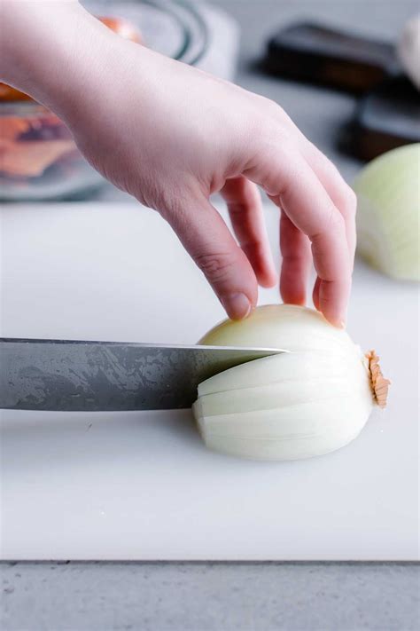 Instructions. Start by slicing the top end of the onion, about ½″ into the bulb of the onion. Keep the root end intact. Place the onion on a cutting board, root end up, and slice vertically through the onion, cutting in half. Take 1 half and peel back the outer skin layers all the way to the root. Place flat-side down and make vertical cuts ...